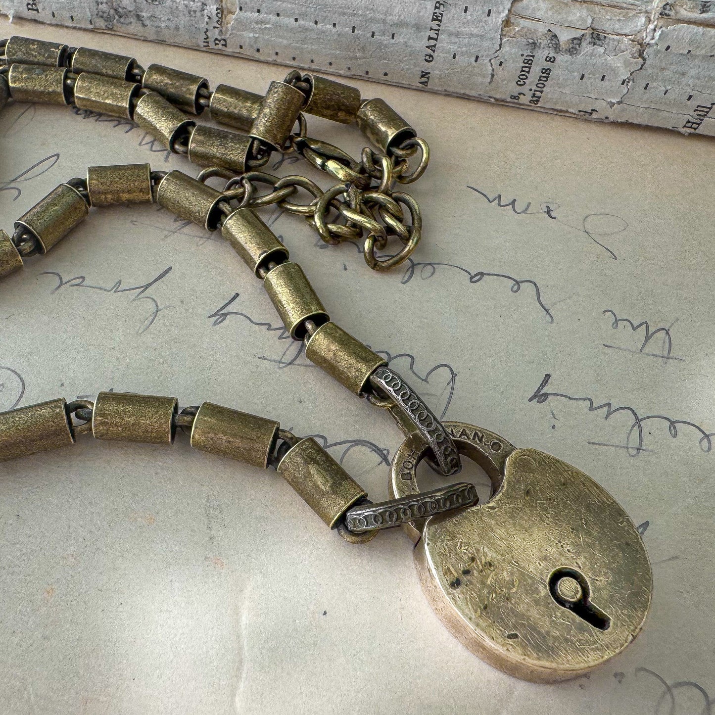 Bronze padlock charm on a chain against a textured background